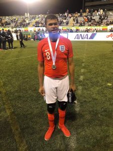 Image shows Rainbow stood on the pitch after representing England with an IBSA Blind Football World Grand Prix silver medal around his neck.