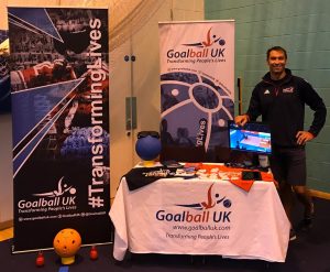 View of a standard Goalball UK stand at a university volunteering fair, with Steve Cox standing and smiling at the side.