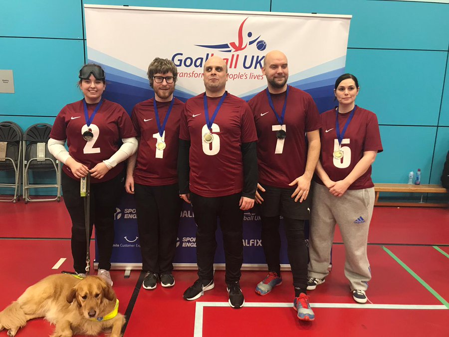 Image shows Gemma stood with her West Yorkshire teammates following a tournament. They are proudly wearing their medals in front of a Goalball UK banner.