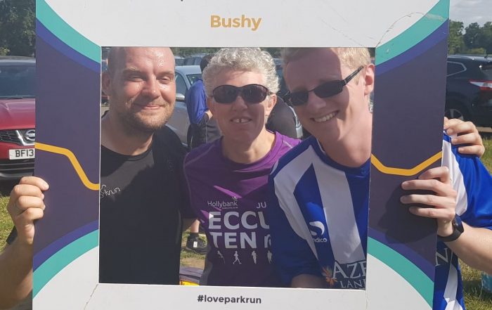 Phil, Kathryn and Stephen at Busy parkrun holding the selfie frame with the parkrun logo and Bushy on it