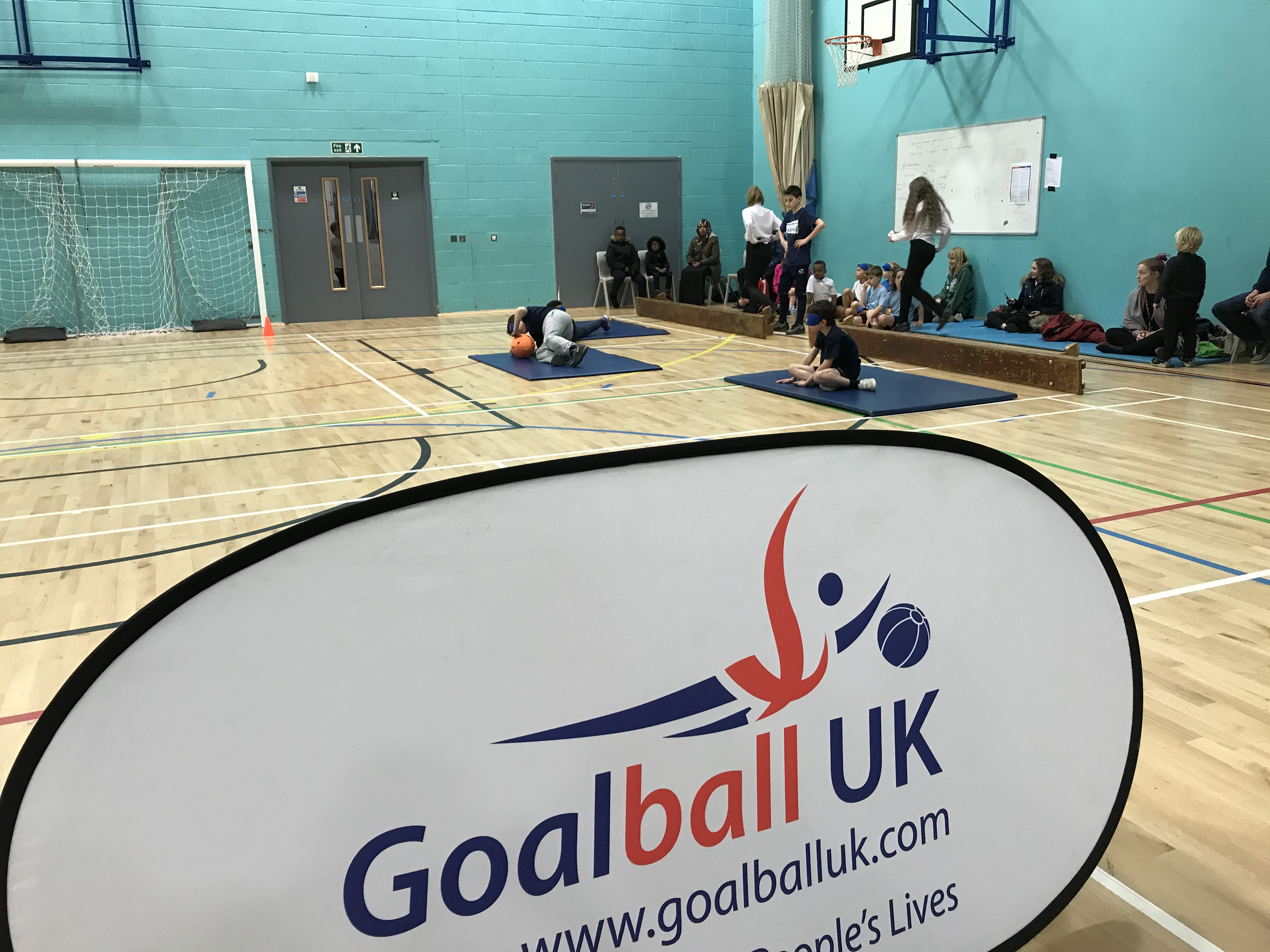 Photo with Goalball UK banner in foreground and school competition in background
