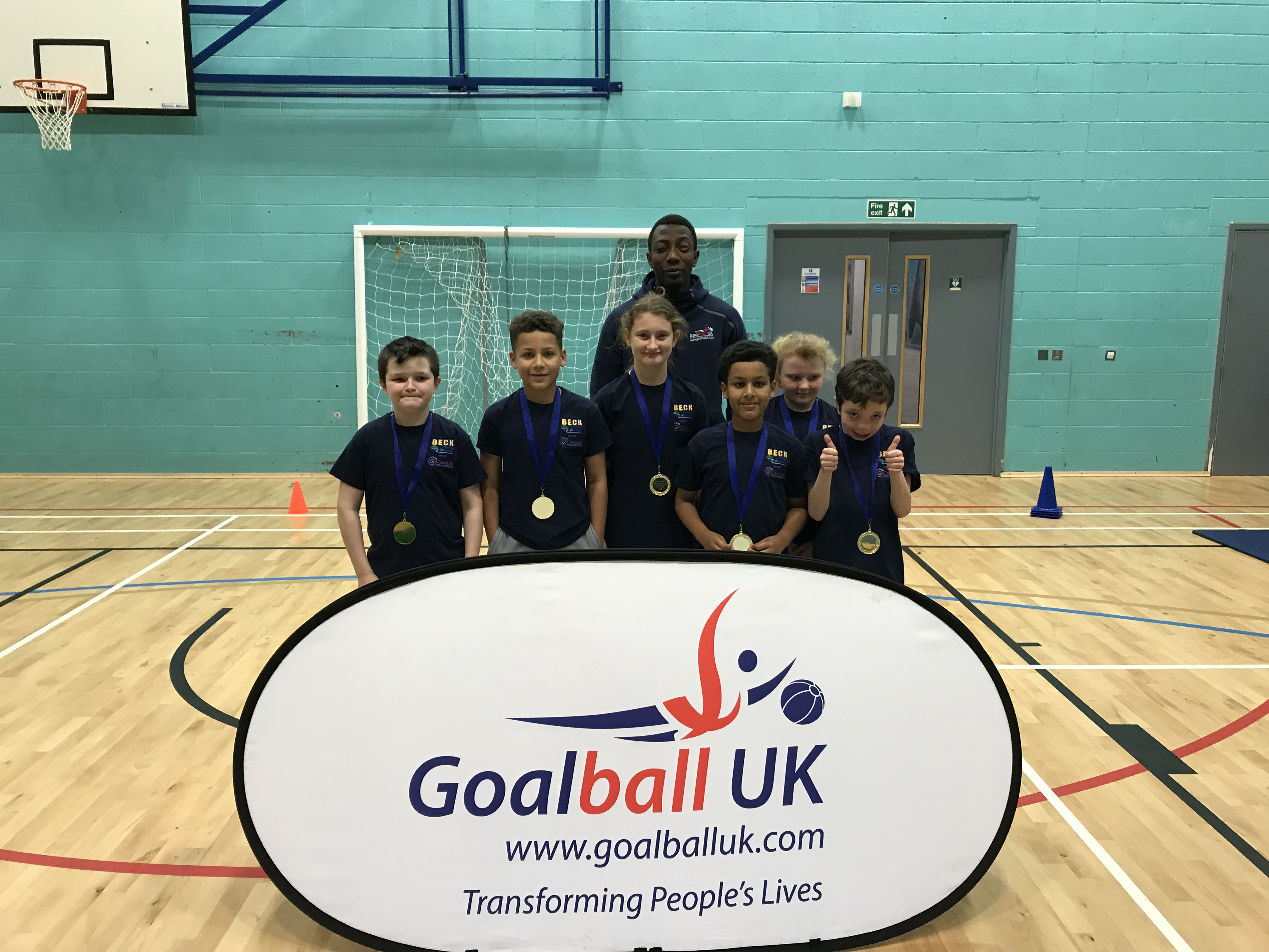 Smiling children with their gold medals from winning at the school competition, with GB player Caleb Nanevie supporting them