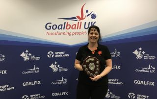 Emma Evans receiving the Keith Lound Award in 2019, smiling and holding the award with a Goalball UK banner in the background.
