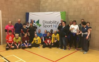 Group photo of everyone at the Norther Ireland Goalball Roadshow, with the Disability Sport Norther Ireland logo on a banner in the background
