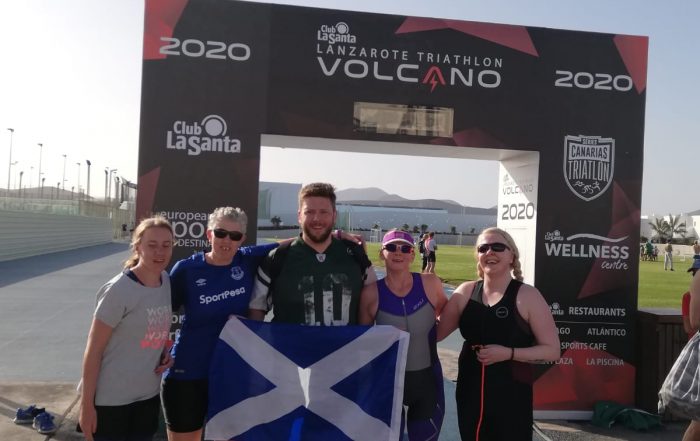 Paul with Scottish teammates proudly holding St. Andrews flag on the finish line of a triathlon