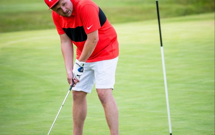 Image shows Nick playing golf, mid put