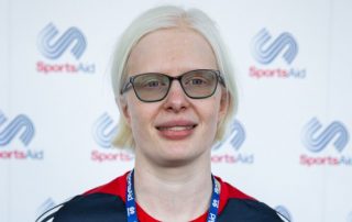 Image shows Sarah Leiter smiling in from of a SportsAid advertising board