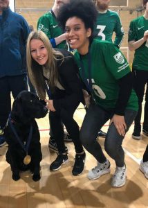 Aneesah and Coach Kirsty posing with a guide dog wearing a medal!