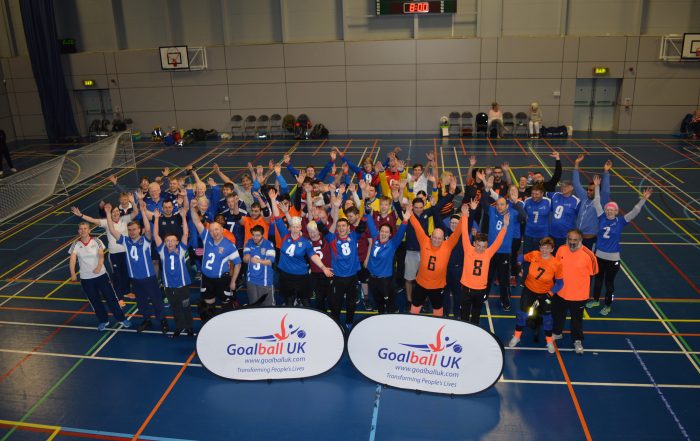 Post tournament photo with the teams in front of a banner putting their hands in the air.