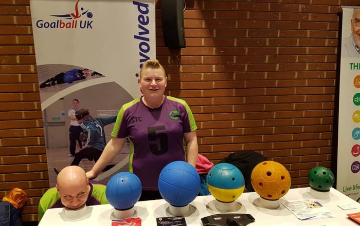 Sally and Tom Britton stood together in Croysutt Warriors kit. Tom is crouched down resting his head on top of some tape!