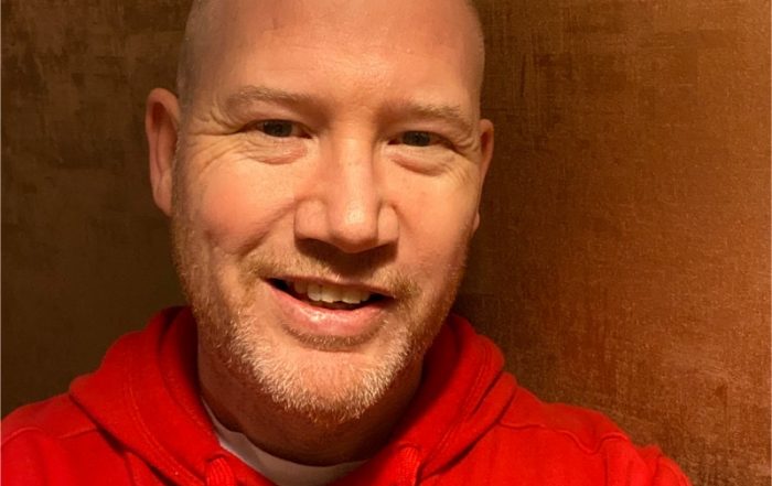 Goalball UK CEO Mark Winder smiling whilst taking a selfie in a red Goalball UK hoodie.