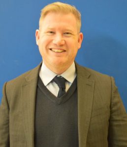 Goalball UK CEO Mark Winder smiling in a brown suit in front of a dark blue background.