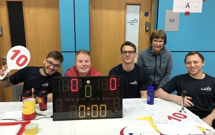 Volunteers at Sheffield North region tournament posing with smiley faces before a goalball game.