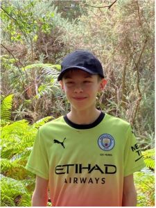 Image shows Bobbie-Jack stood smiling at the camera wearing his Manchester City football shirt