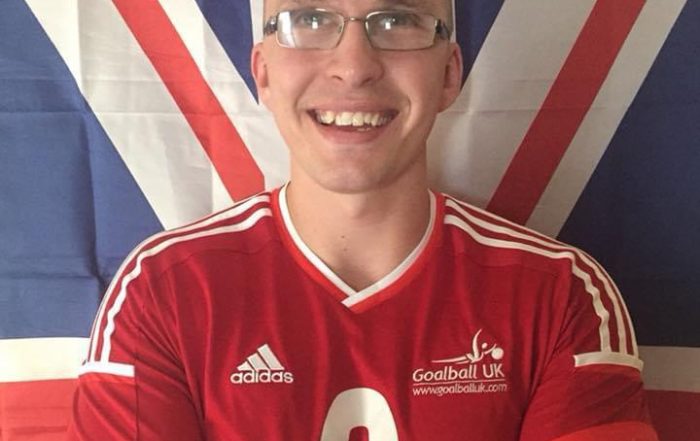 Image shows Matt Loftus stood smiling at the camera with his arms crossed wearing his GB Mens jersey