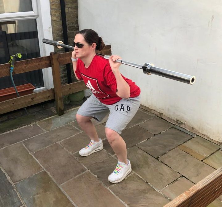 Image shows Gemma working out in her garden, she is part way through performing a squat