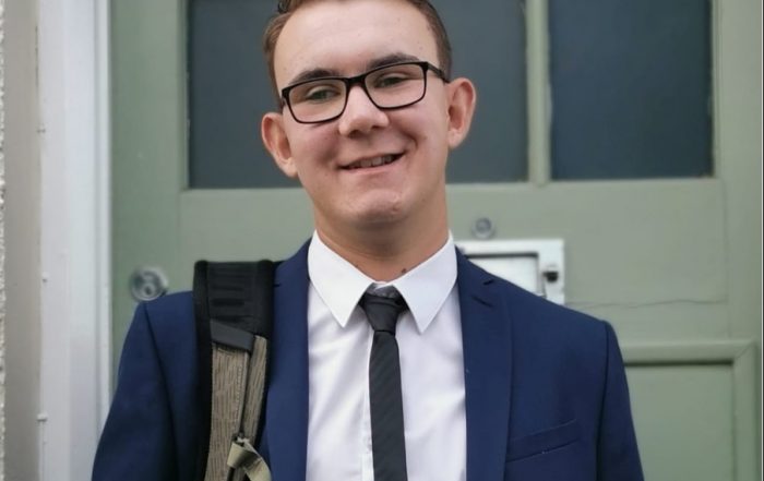 Image shows Jacob stood wearing a suit. He is smiling at the camera with his hands in his pockets.