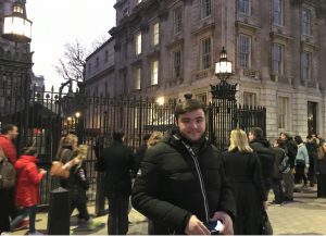 Image shows Max Mackenzie stood on a street in front of lots of people, smiling at the camera