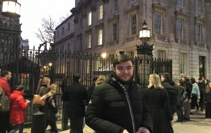 Image shows Max Mackenzie stood on a street in front of lots of people, smiling at the camera