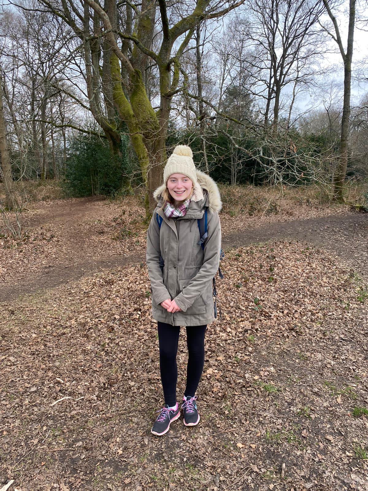 Phoebe stood in the woods wearing a big coat and a woolly hat