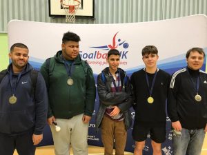 Image shows Abdul stood with his RNC academy teammates after a goalball tournament. They are all stood proudly with their medals in front of a Goalball UK banner.