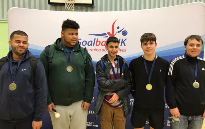 Image shows Abdul stood with his RNC academy teammates after a goalball tournament. They are all stood proudly with their medals in front of a Goalball UK banner.