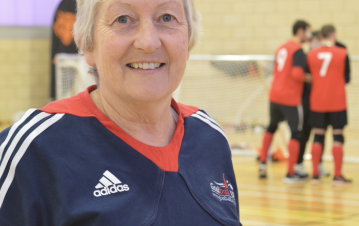 Image shows Judith stood wearing her Goalball UK t-shirt smiling at the camera