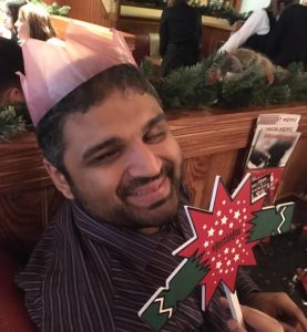 Image shows Bilal in a restaurant smiling holding up a Christmas cracker sign