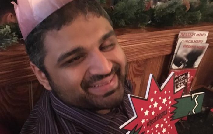 Image shows Bilal in a restaurant smiling holding up a Christmas cracker sign