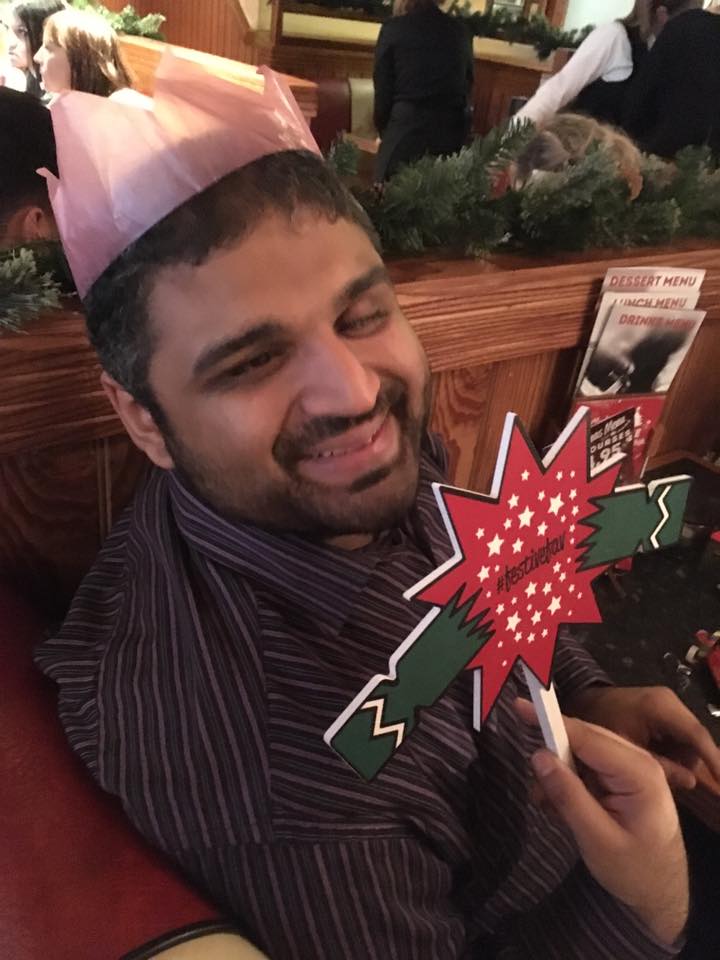 Image shows Bilal in a restaurant smiling holding up a Christmas cracker sign