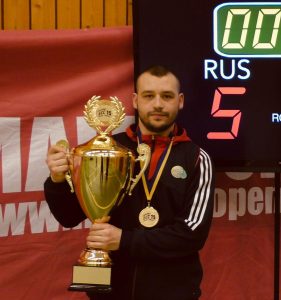 Image shows Dave Butler at the European Championships in front of a scoreboard, holding a trophy