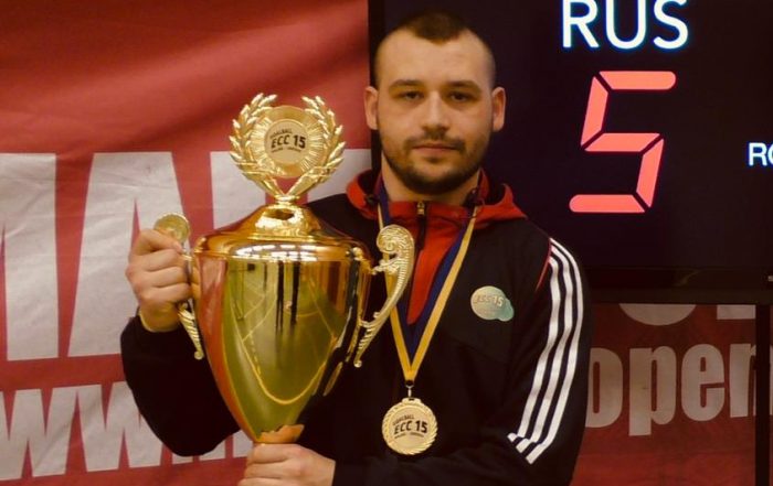 Image shows Dave Butler at the European Championships in front of a scoreboard, holding a trophy