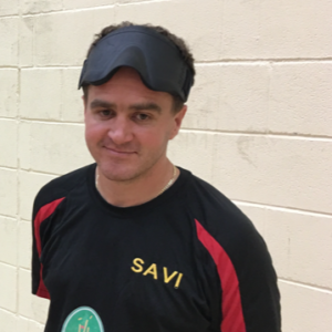 image shows Matt Cliff smiling at the camera after playing goalball with his eyeshades on his head