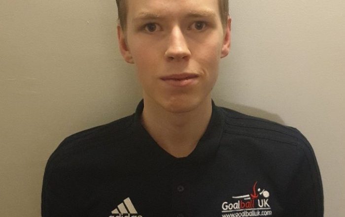 Image shows Stuart Hudson kneeling on the floor with his hands on his lap, looking at the camera