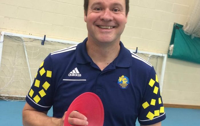 Image shows Tom Evison wearing his Winchester Goalball Club top, stood smiling at the camera and holding a red training cone