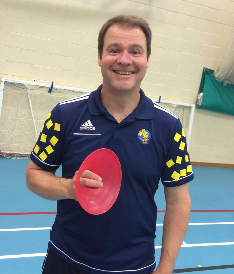 Image shows Tom Evison wearing his Winchester Goalball Club top, stood smiling at the camera and holding a red training cone