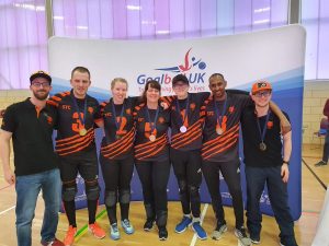 Image shows Georgie Bullen stood with her Fen Tigers teammates in front of a Goalball UK banner