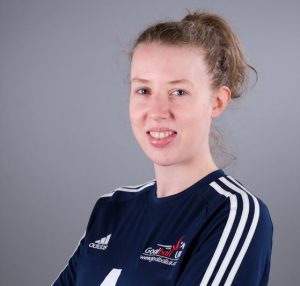 Image shows Georgie Bullen stood smiling at the camera with her arms crossed. She is wearing her GB womens kit