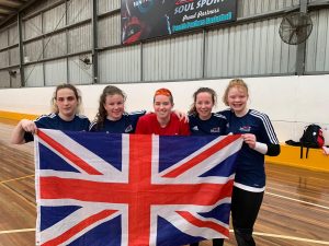 Image shows Nansi Stood with her GB under 19 teammates holding a union jack flag