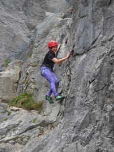 A climber, wearing a helmet and harness, traversing a rock face