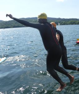 Two swimmers, wearing wetsuits, jumping off a pier into a lake