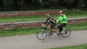 Fran and Dean (from WY) riding a tandem along a road on the Goalball UK Coast to Coast (2015)
