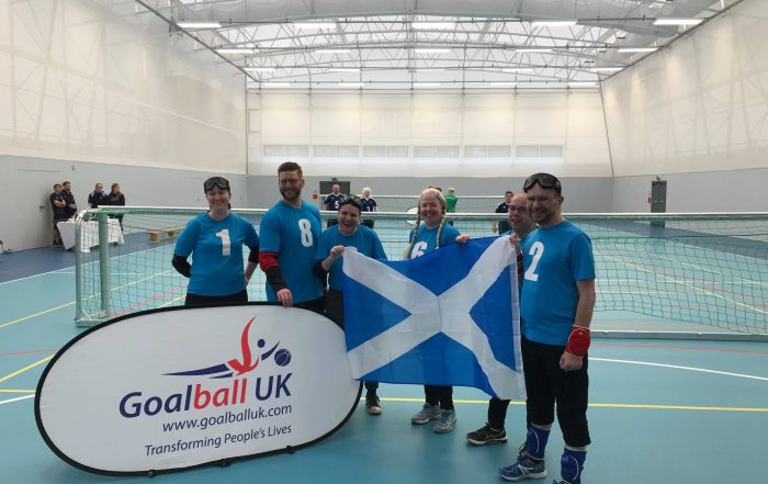 Glasgow goalball team stood as a group with a Scotland flag at the Home Nations Tournament in 2018.