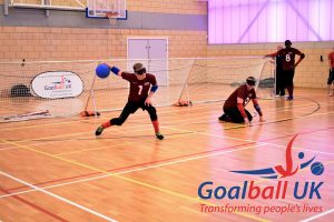 Peter Doyle shooting a goalball at an elite tournament in Longbridge, Birmingham with Matt Loftus in centre and Caleb Nanevie on the left wing.