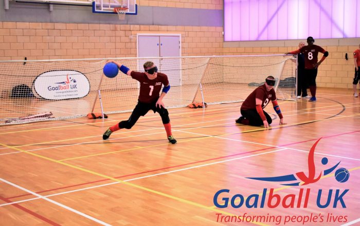 Peter Doyle shooting a goalball at an elite tournament in Longbridge, Birmingham with Matt Loftus in centre and Caleb Nanevie on the left wing.