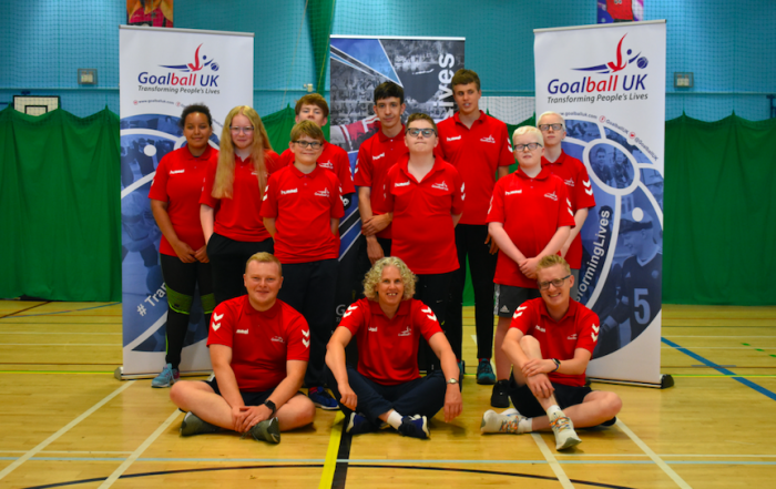 Summer Camp 2021 group photo. All wearing red summer camp shirts in front of Goalball UK banners.