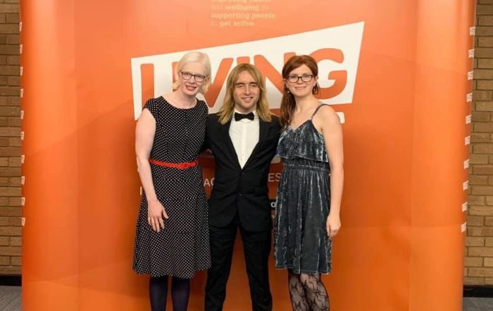 Sarah Leiter, Warren Wilson and Emily Watton stood together in formal attire in front of an orange background at an awards ceremony.