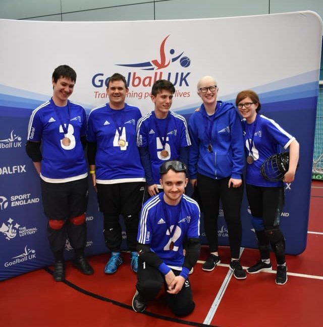 A group photo of an Intermediate team of Cambridge Dons in front of a Goalball UK banner.