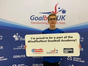 Harry Bainbridge in his Goalball Academy shirt holding up a sign which reads "I'm proud to be a part of the #FindTheNext Goalball Academy".