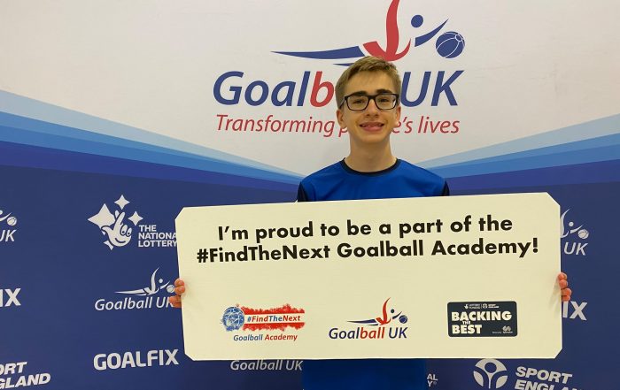 Harry Bainbridge in his Goalball Academy shirt holding up a sign which reads "I'm proud to be a part of the #FindTheNext Goalball Academy".